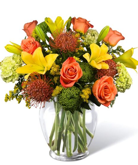  Roses, hydrangea, lilies, and pin cushion protea in a clear glass vase..